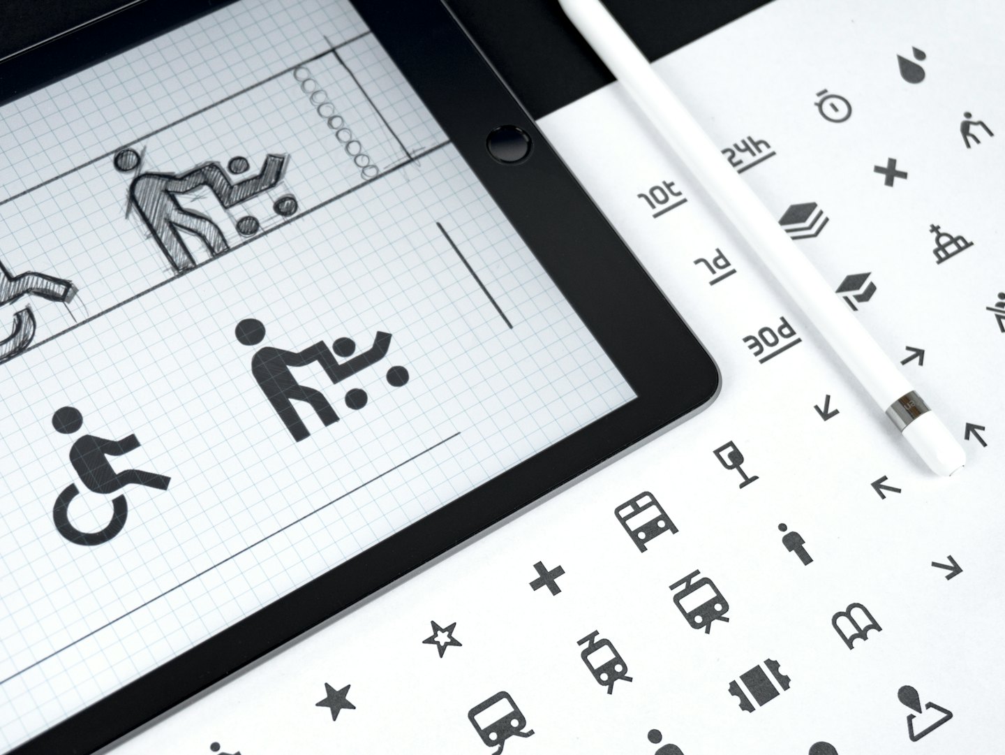Tablet displays graphic design concepts next to stylus and icon sheet.